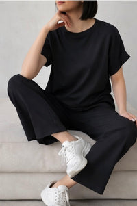 Person wearing a black outfit with white sneakers sitting on a light-colored surface.