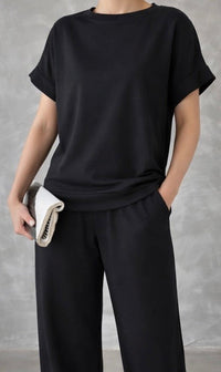 Person wearing a black outfit holding a folded white garment against a gray background