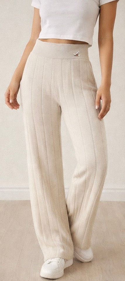 Person wearing beige pleated pants and white sneakers on a plain background