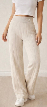 Person wearing beige pleated pants and white sneakers on a plain background