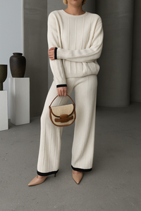 Person wearing a white outfit holding a woven handbag in a minimalistic setting