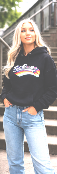 A woman wearing a black hoodie with a colorful 'Be Smitty' graphic on the chest, paired with light blue jeans, standing outdoors on steps.