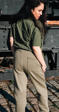 Person wearing a green T-s and beige pants standing in front of a large black vehicle on a brick surface.