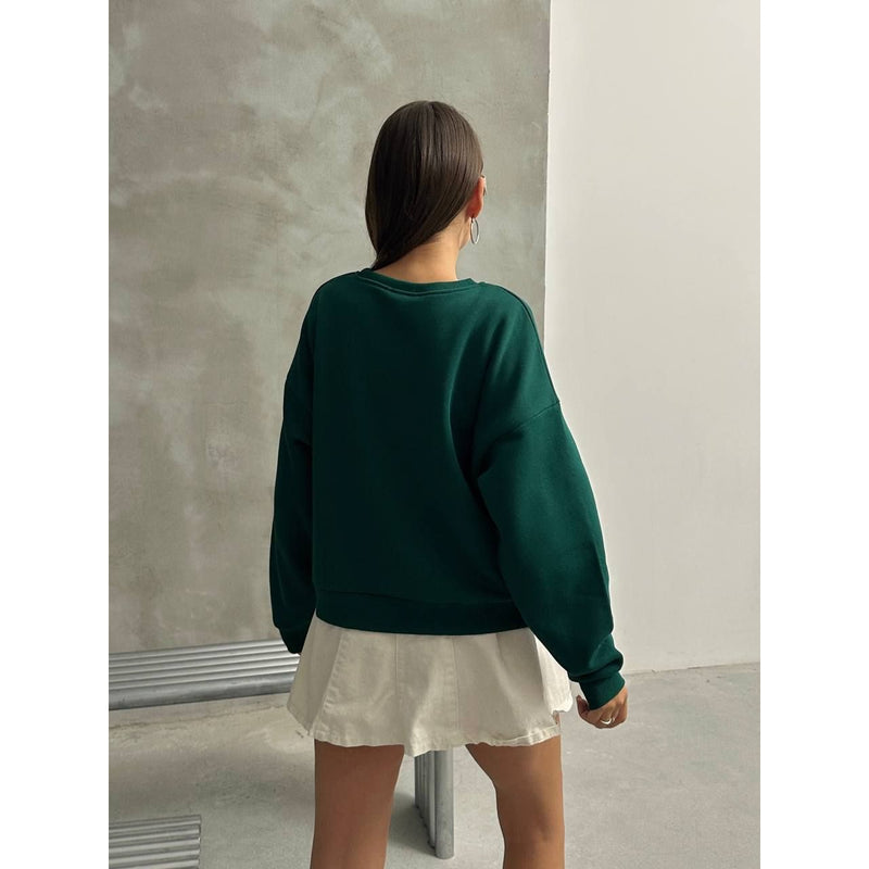 Person wearing a green sweatshirt and white skirt against a plain wall.