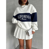 Person wearing a white and black 'California' sweatshirt with a pleated skirt against a gray background