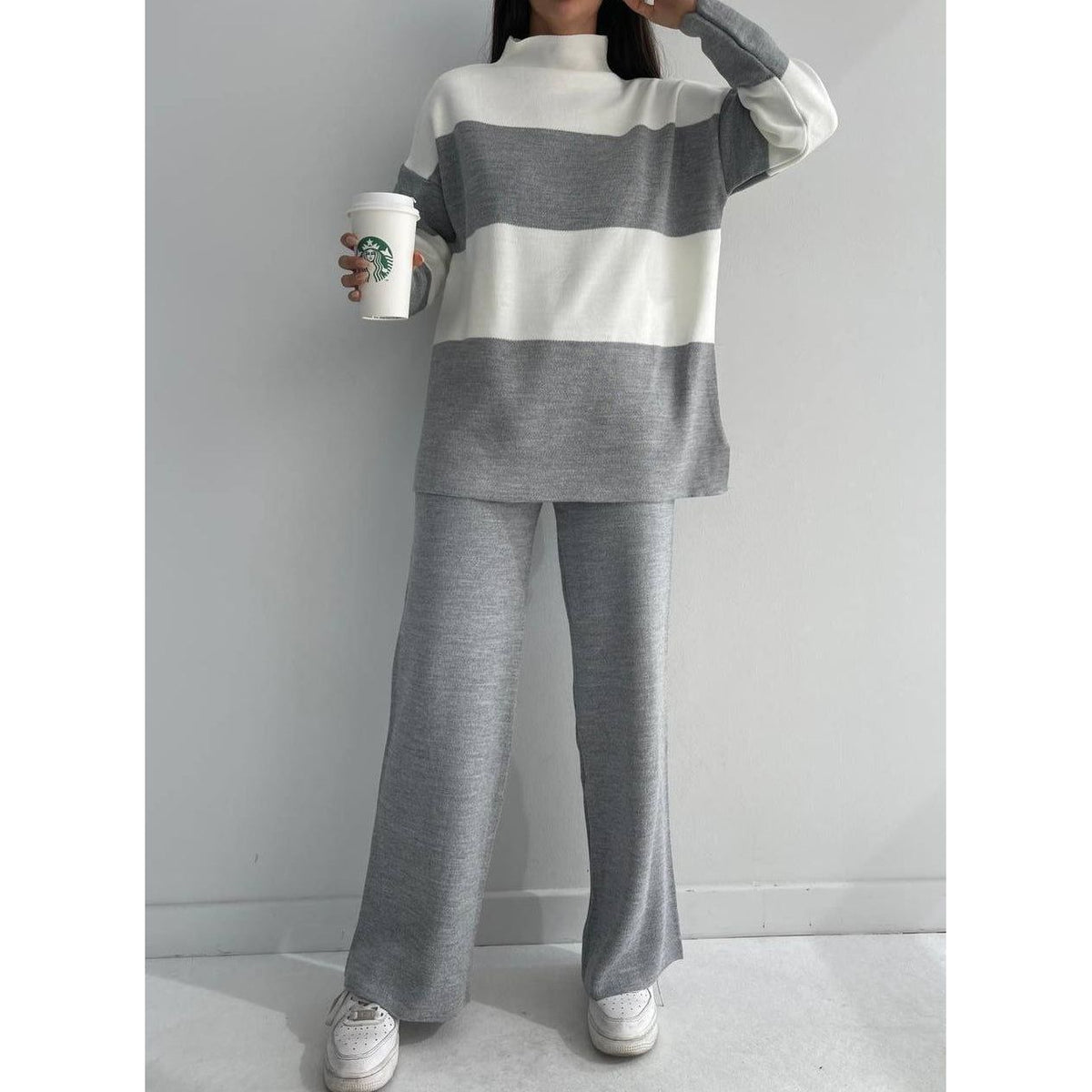 Person wearing a grey and white striped sweater with wide-leg pants, holding a Starbucks cup.