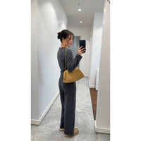 Woman taking a mirror selfie wearing a gray outfit and yellow handbag in a hallway.