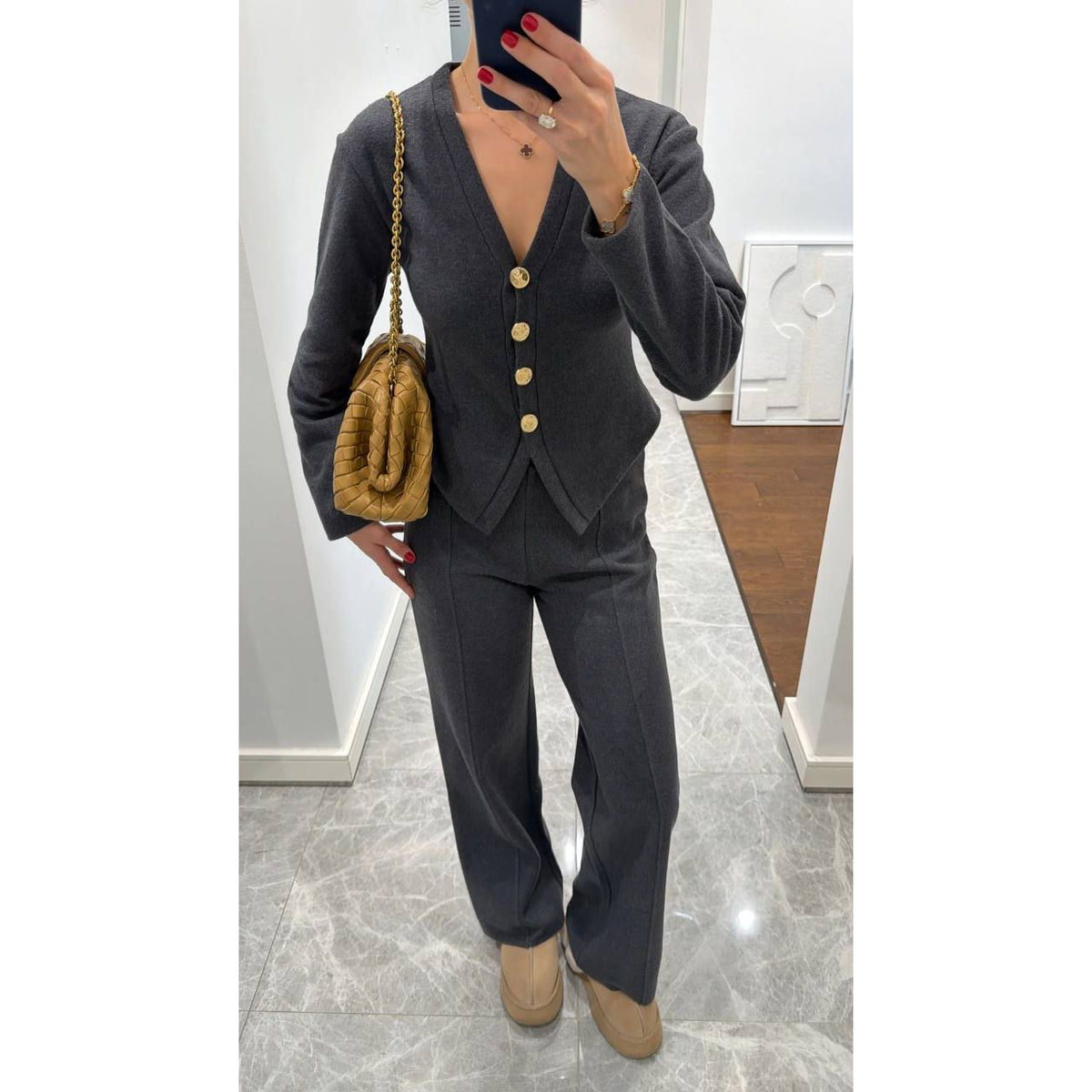 Person wearing a gray suit with gold buttons, holding a brown fur bag indoors.