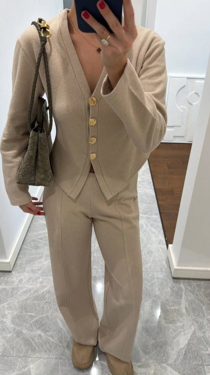 Person wearing a beige suit with a matching handbag indoors.