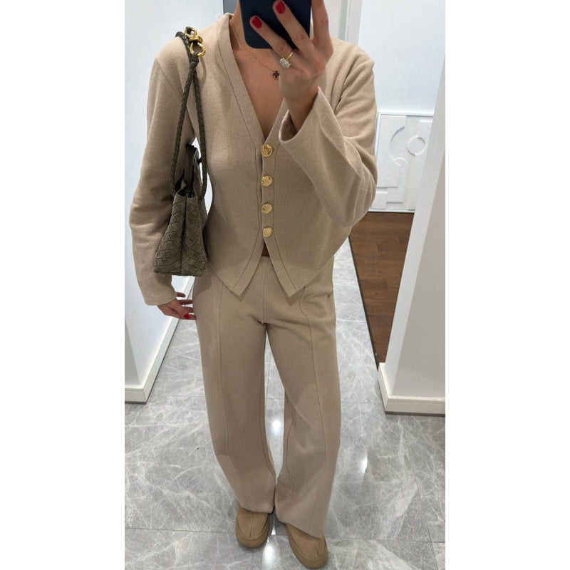 Person wearing a beige suit with a matching handbag indoors.