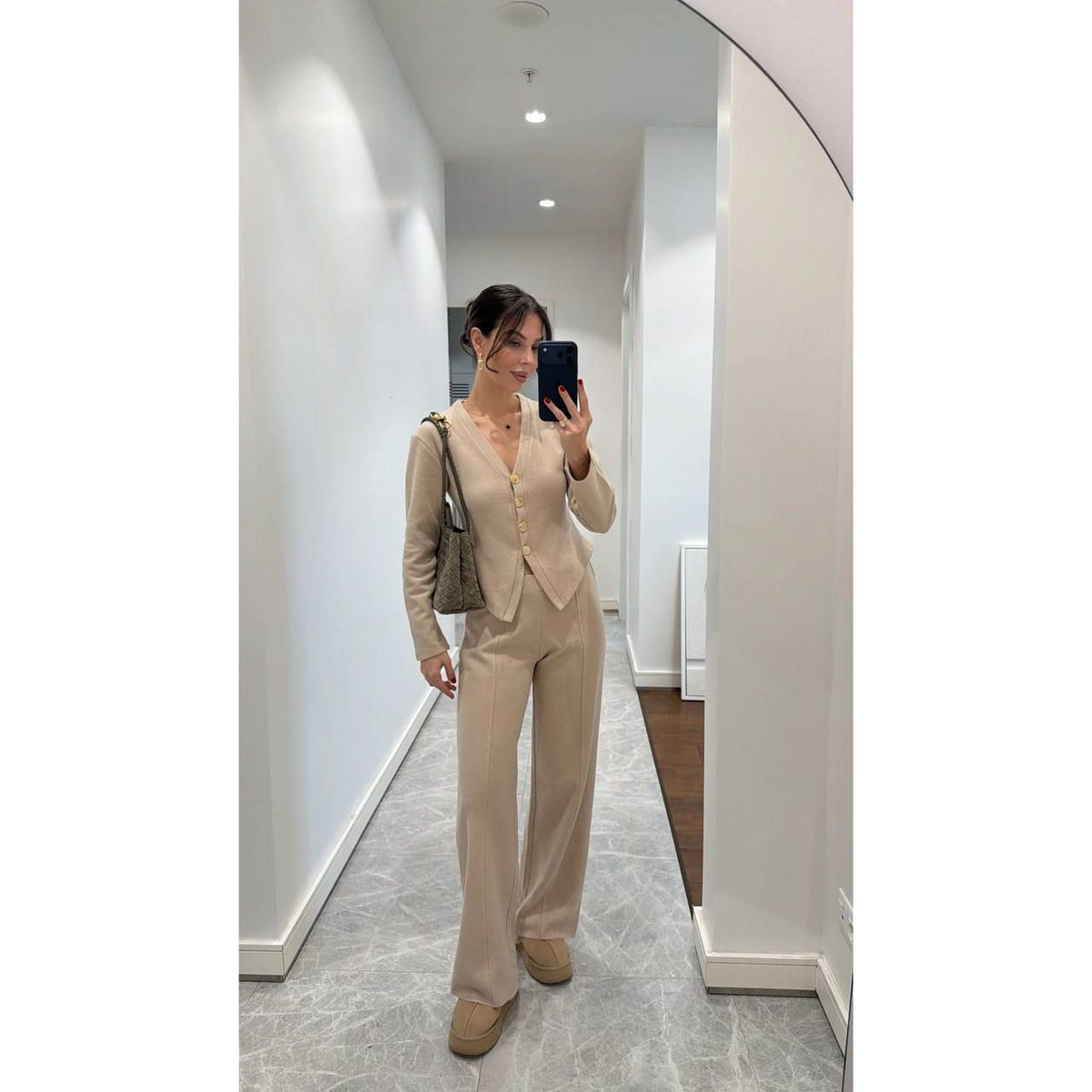 Woman taking a mirror selfie wearing a beige suit in a hallway.