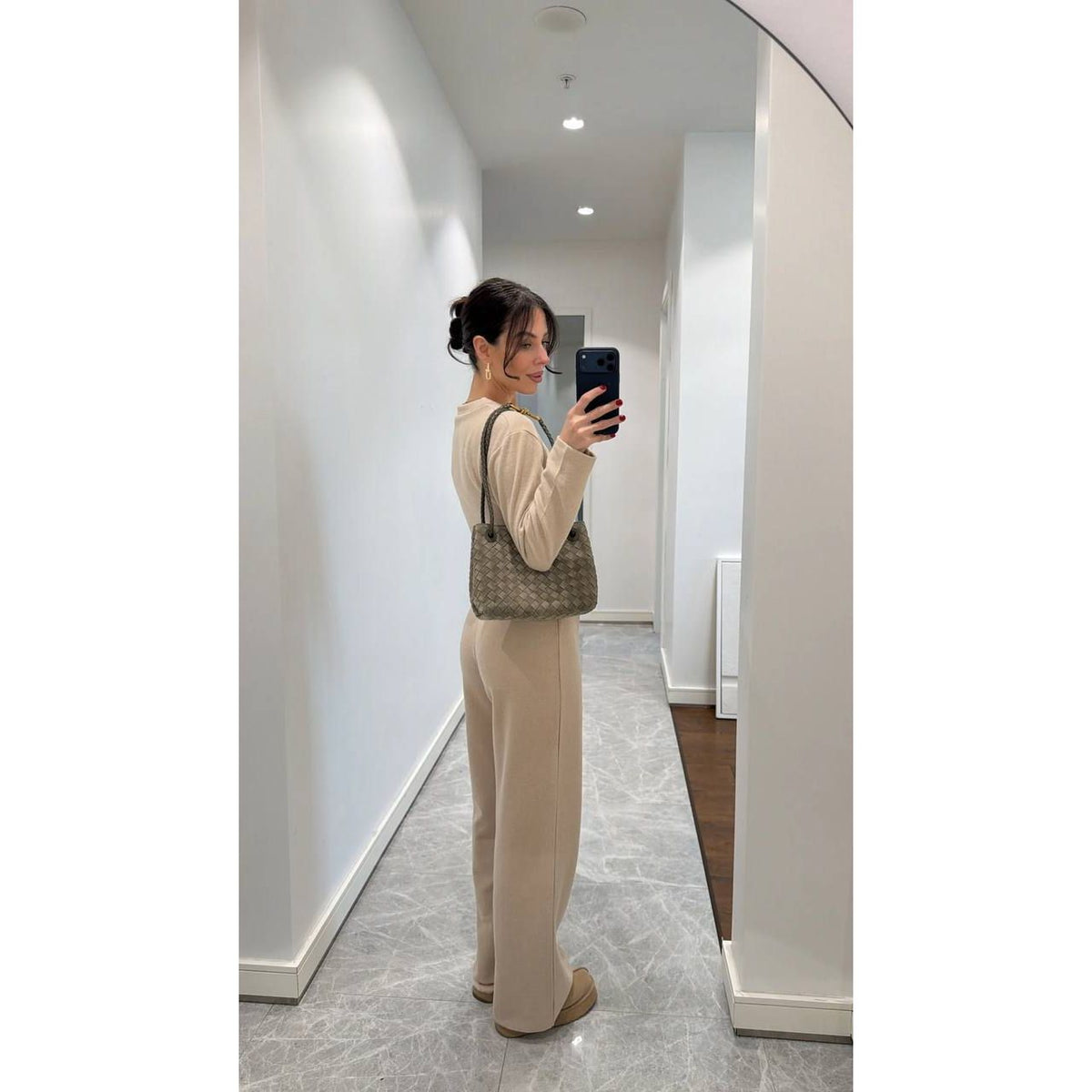 Person taking a mirror selfie wearing a beige outfit and holding a green handbag.