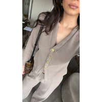 Person wearing a beige  cardigan with gold buttons, holding a brown handbag.