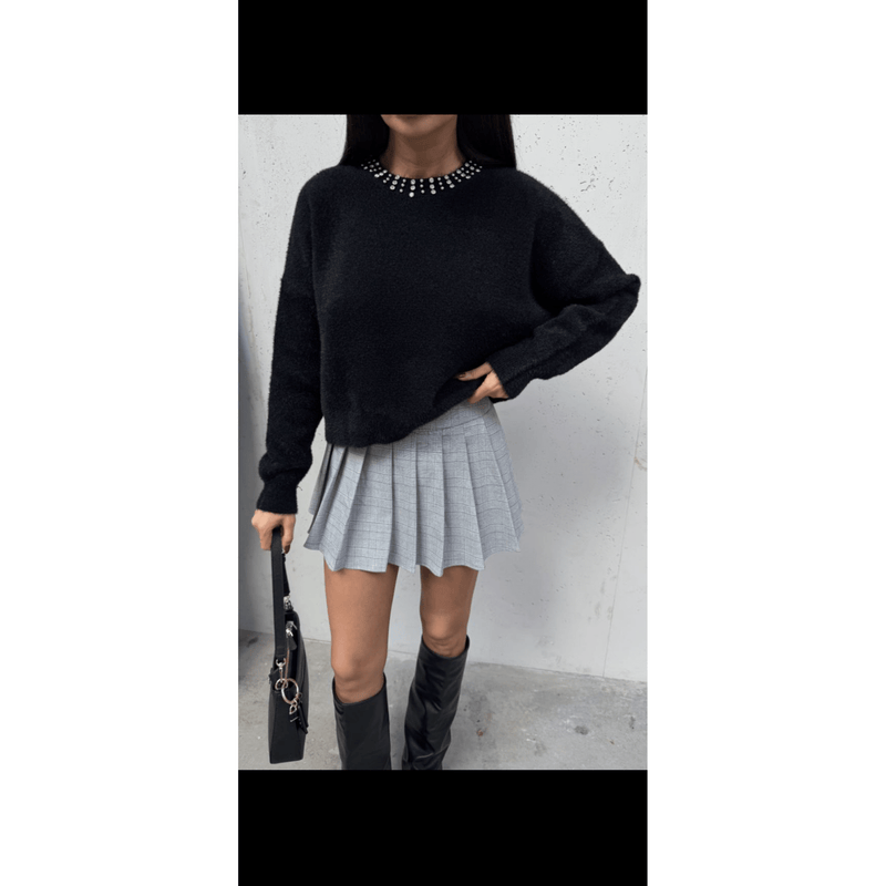 Person wearing a black sweater, gray plaid skirt, and black knee-high boots against a white wall.