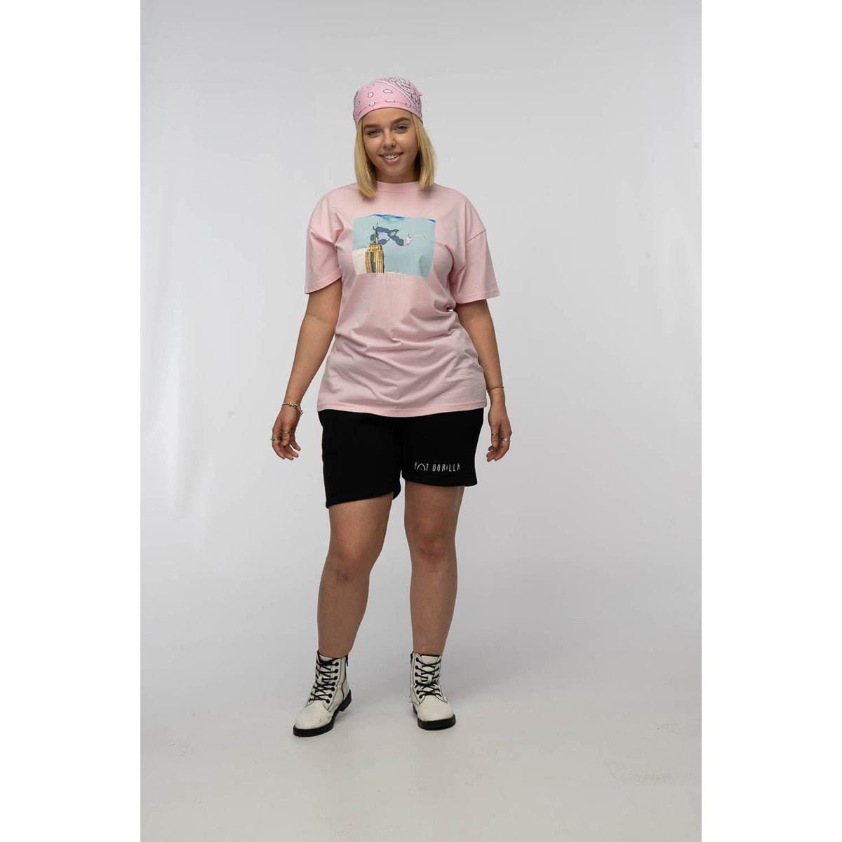 Person wearing a pink graphic t-shirt, black shorts, and white sneakers on a plain background