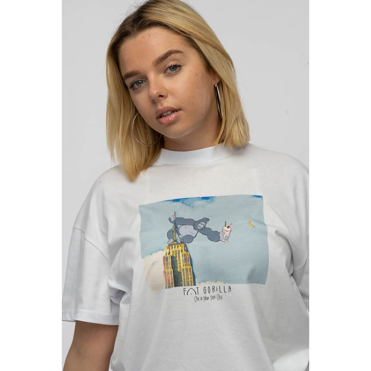 Person wearing a white t-shirt with a graphic design on a plain background