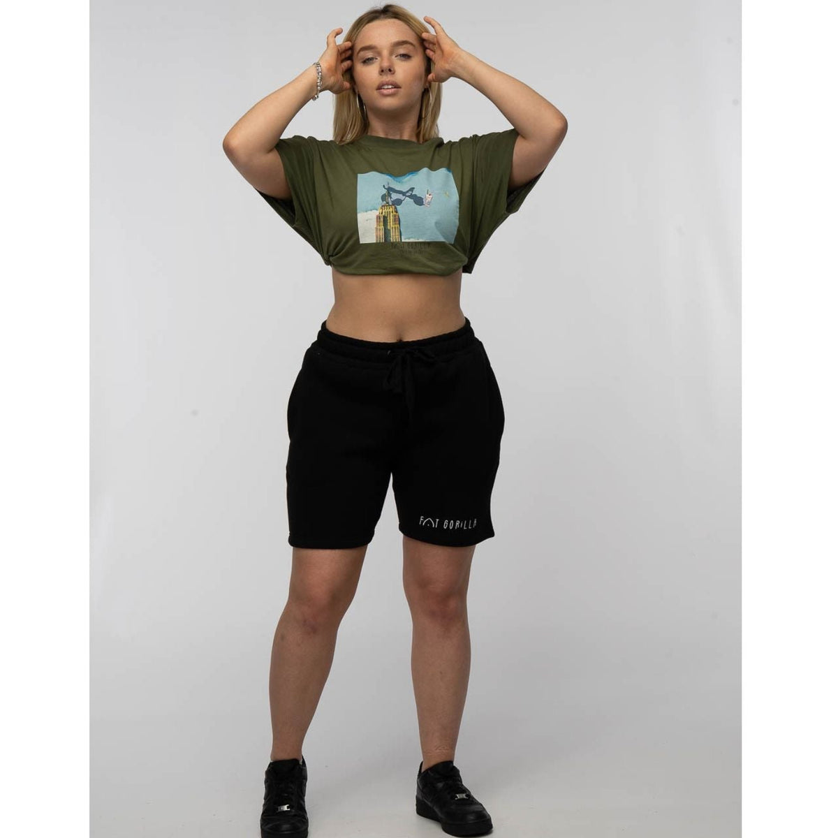 Woman wearing a green crop top with a graphic design and black shorts on a white background