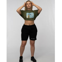 Woman wearing a green crop top with a graphic design and black shorts on a white background