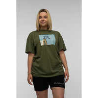 Person wearing an olive green t-shirt with a graphic design on a plain background