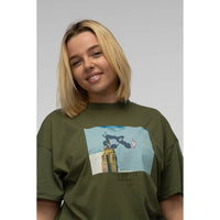 Person wearing a green t-shirt with a graphic design on a plain background