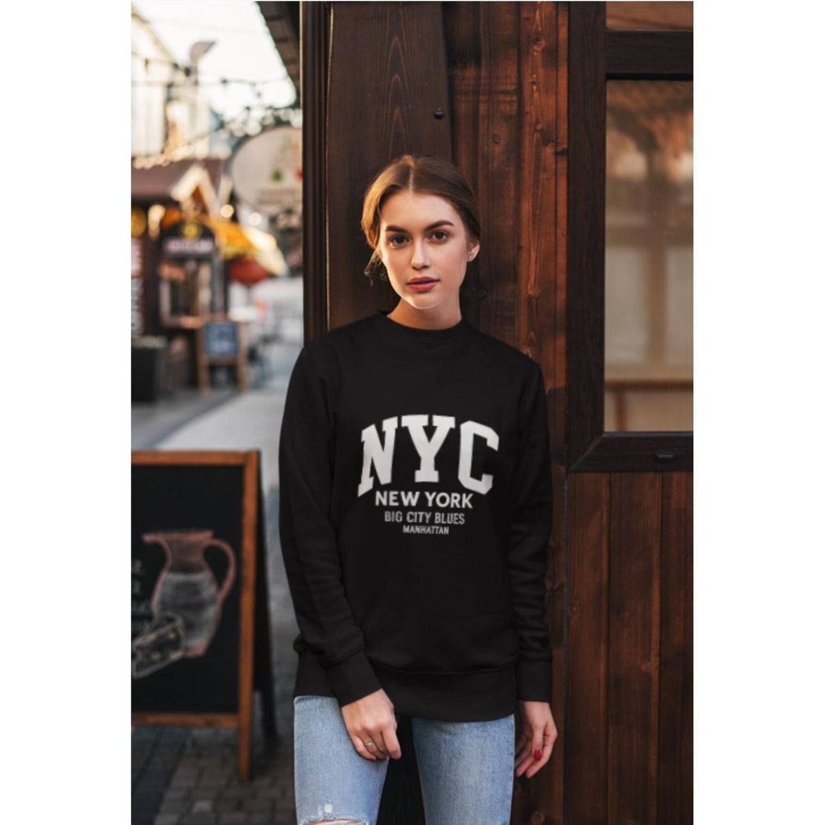 Woman wearing a black sweatshirt with 'NYC New York Big City Blues' text, standing in an urban setting.