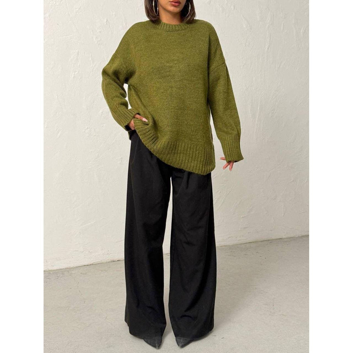 Person wearing a green sweater and black pants against a white background