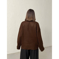 Person wearing a brown sweater against a plain white wall