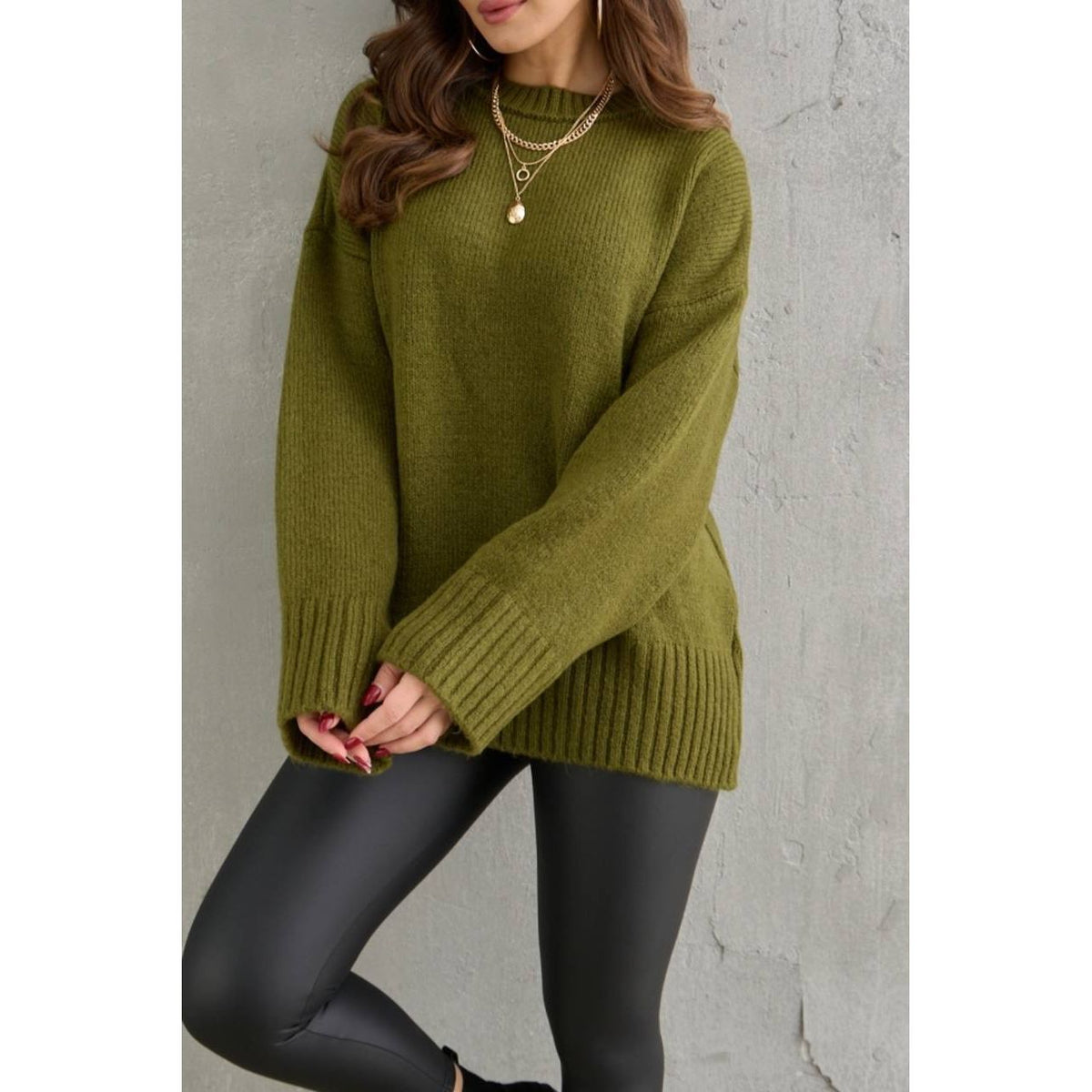 Person wearing a green sweater and black leggings against a gray background