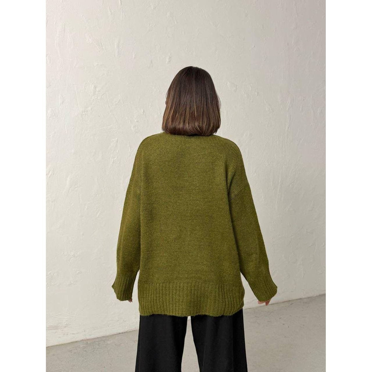 Person wearing a green sweater against a white wall