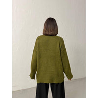 Person wearing a green sweater against a white wall