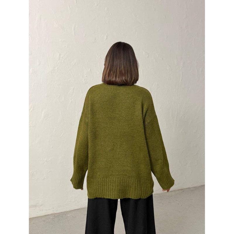 Person wearing a green sweater against a white wall