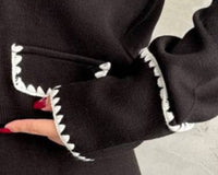 Black cardigan with white trim on a textured gray background