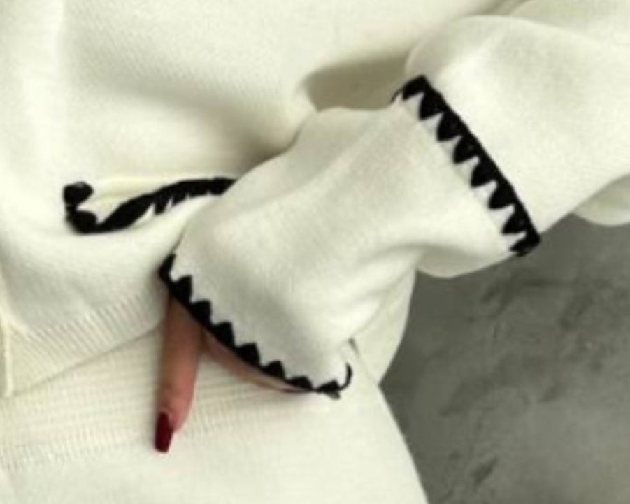 White cardigan with black trim worn by a person on a gray background