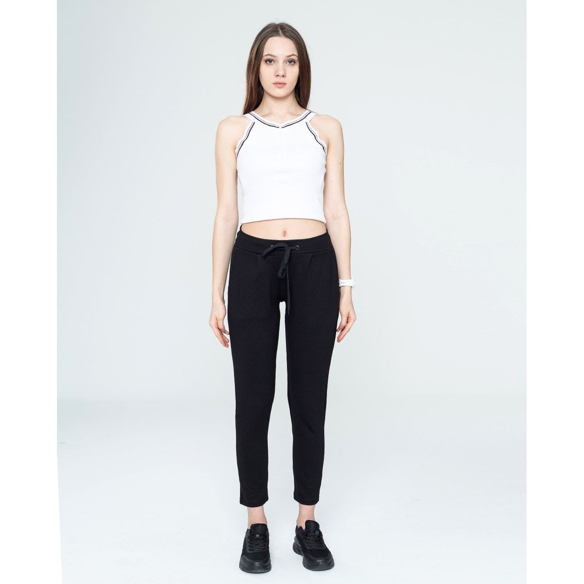 Woman wearing a white crop top and black pants on a white background