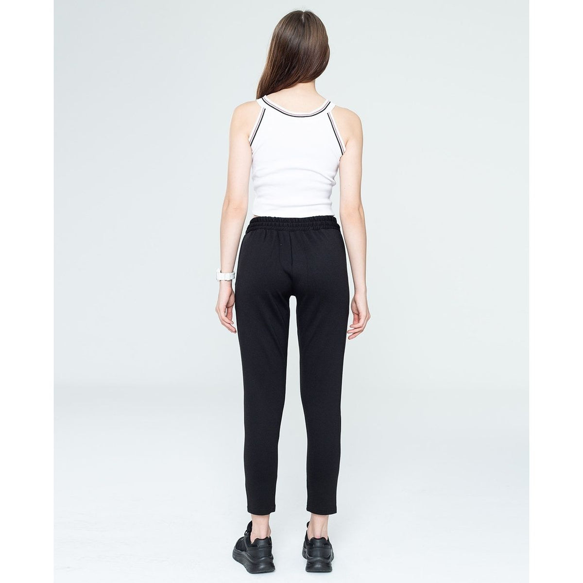 Woman wearing a white tank top and black pants on a plain background