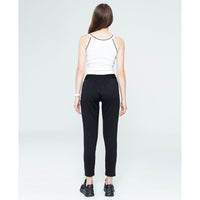 Woman wearing a white tank top and black pants on a plain background