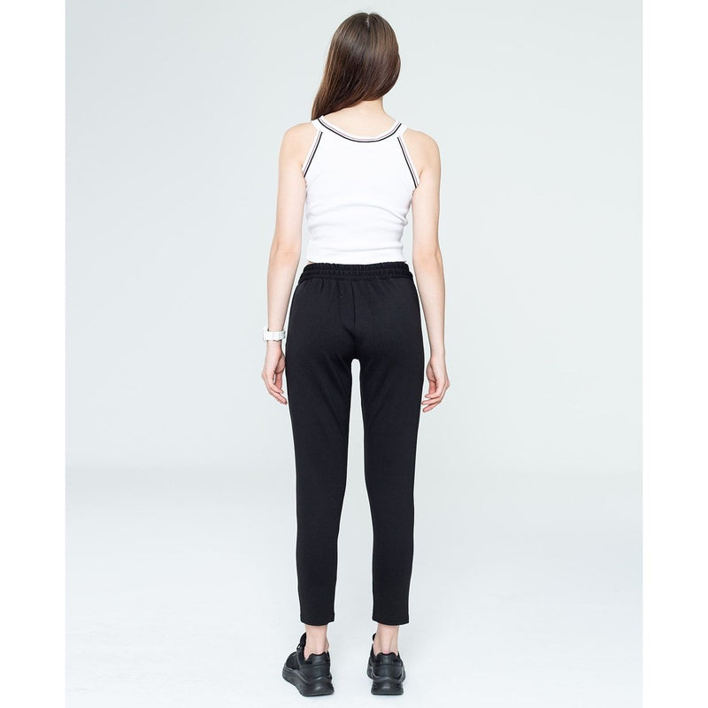 Woman wearing a white tank top and black pants on a plain background