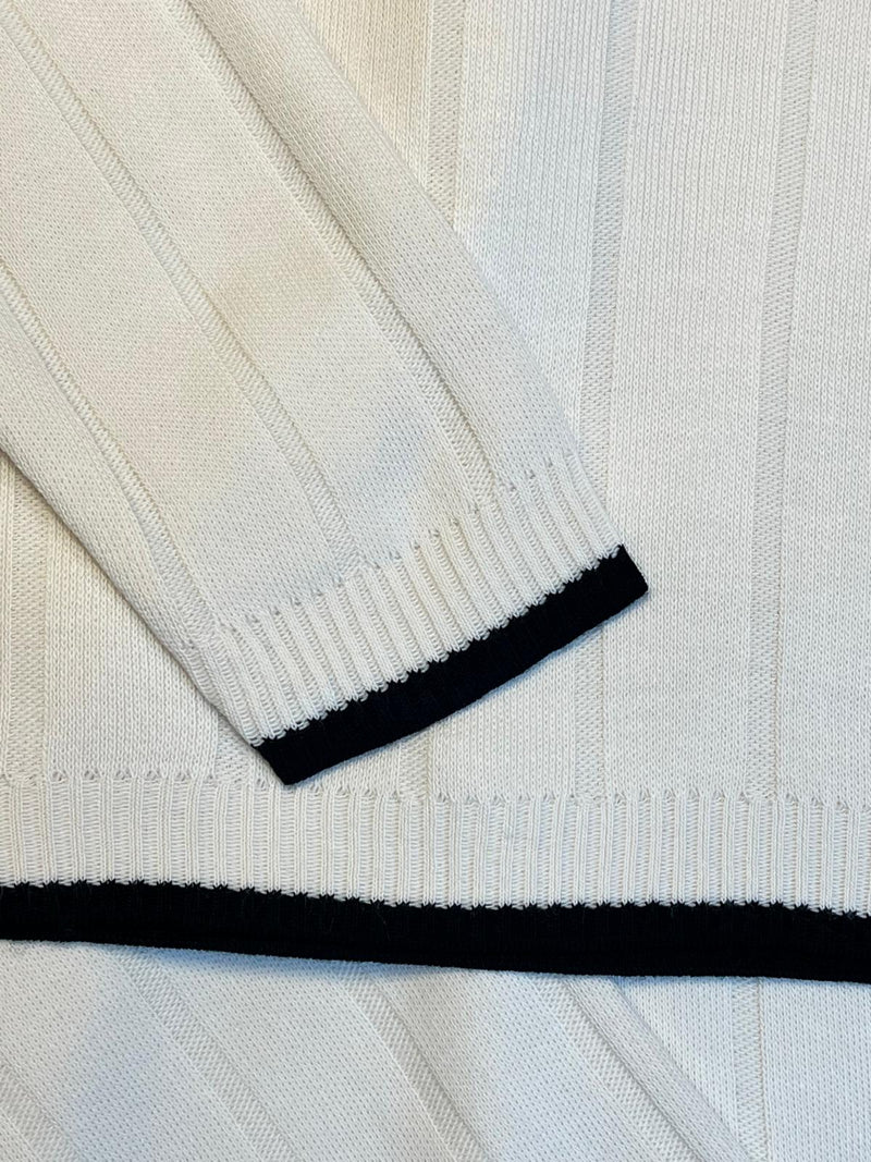 Close-up of a white sweater with black trim on a light gray background